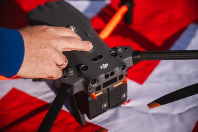 Hand am Gehäuse einer DJI-Drohne auf dem Landeplatz beim Vorflugcheck