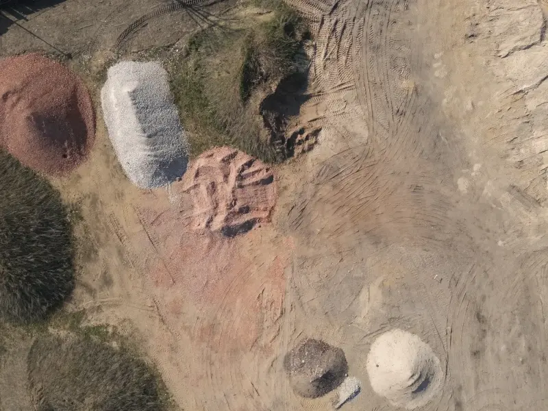 Mehrere Haufwerke aus Sand, Kies und Ziegelbruch auf einem Lagerplatz von oben